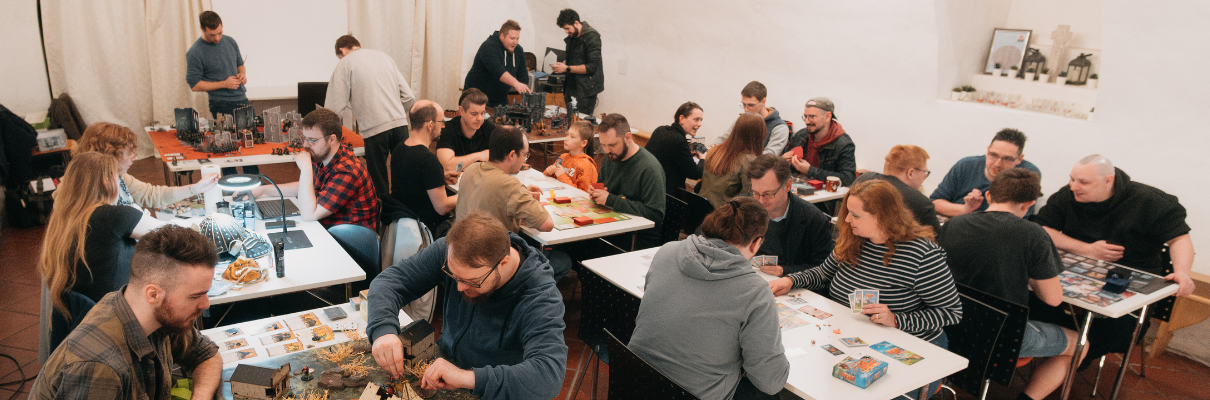 Menschen unterschiedlichen Alters spielen gemeinsam Brett- und Kartenspiele an mehreren Tischen in einem gemütlichen Raum.