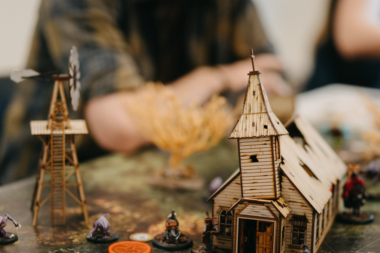 Nahaufnahme eines Malifaux-Geländes. Ein Windrad und eine Kirche in Holzoptik.
