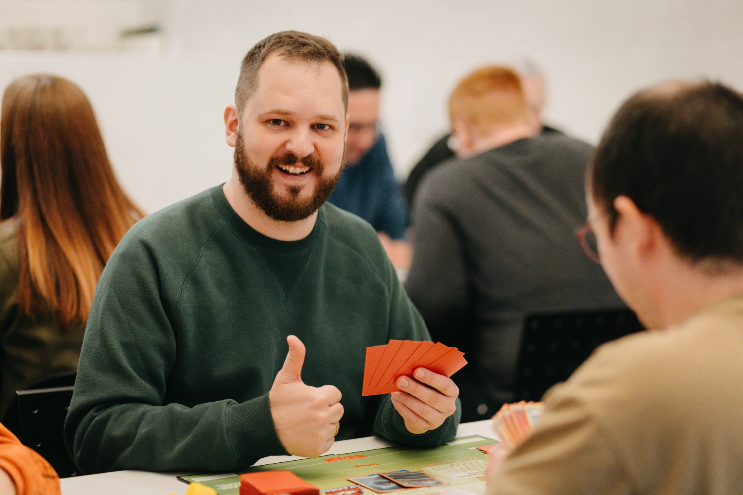 Lächelnder Spieler hält Spielkarten in der Hand und gibt ein Daumen hoch in die Kamera.