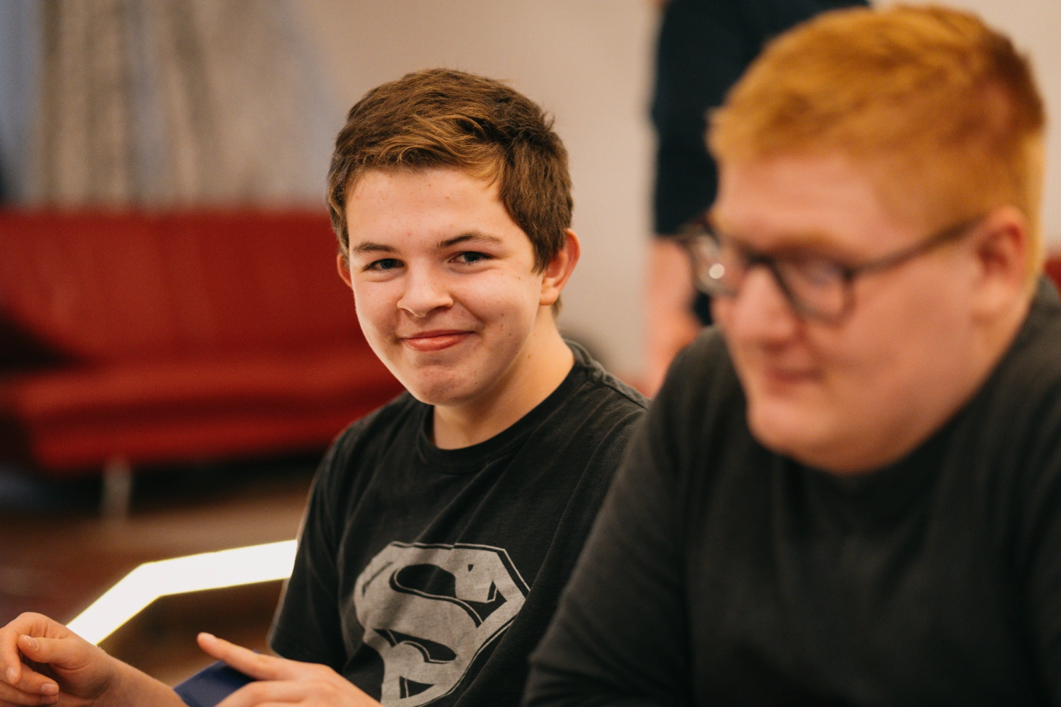 Ein Teenager lächelt in die Kamera. Eine zweite Person ist verschwommen dargestellt daneben.